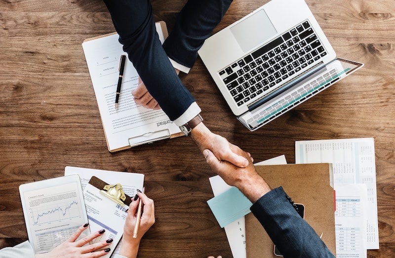 Twee zakenpartners geven elkaar een hand boven een tafel met laptop en documenten